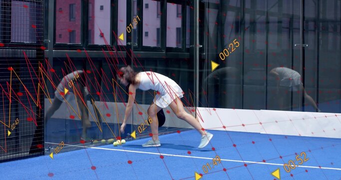 Bending female athlete in white dress picking up yellow balls on blue court, with digital overlay