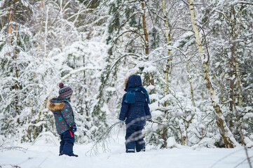 Two young children enjoying active winter day outdoors in snowy forest. Kids play, explore nature, ride a sled, and have fun among snow-covered trees.