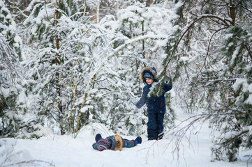 Two young children enjoying active winter day outdoors in snowy forest. Kids play, explore nature, ride a sled, and have fun among snow-covered trees.