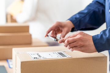 Hands of an anonymous businessman using a smartphone to scan the barcode code on the package label at warehouse