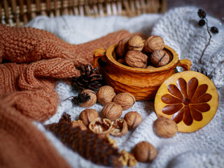 Walnuts in wooden bowl with wooden lid on knitted textile background. Concept of cozy rustic food still life, warm seasonal background with copy space for packaging, banner, social media.