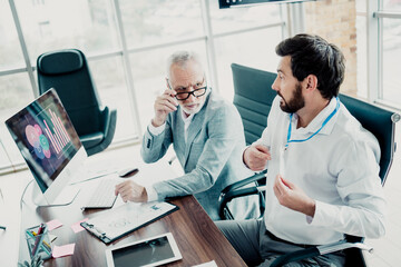 Obraz premium Two businessmen meet in modern office discussing data on computer charts with a colleague and tablet in a collaborative work scene