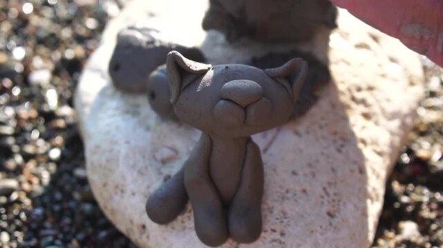 Sculpting clay cat hands create cute animal figure from natural mud on a sunny pebble beach