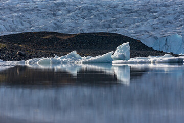 Icebergs drift in quiet harmony across Jökulsárlón glacier lake as soft evening light settles over Southern Iceland’s rugged dark ridges and the distant glacier shimmering behind them © lightcaptured