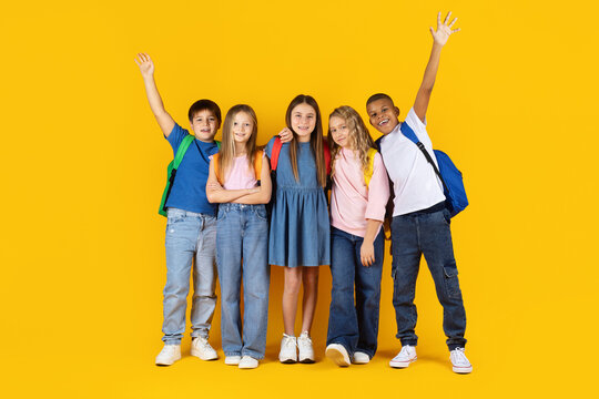 Group of preteen pupils standing together and smiling on yellow studio background. Friendly atmosphere highlights diversity, education, school life, and childhood lifestyle