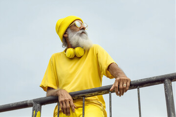 Senior man in yellow beanie and headphones looking thoughtfully against a light sky