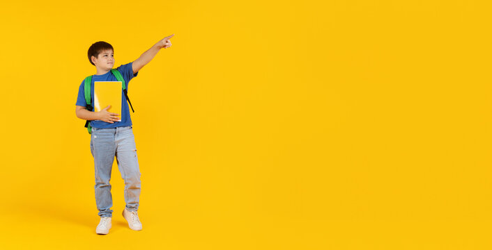 Preteen boy standing with notebook and backpack, pointing upward on yellow studio background. Concept of dreams, imagination, education and future planning