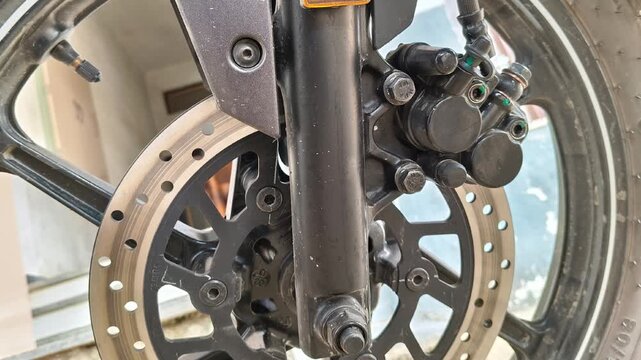 Close up of a motorcycle front hydraulic disc brake system with black caliper and alloy wheel