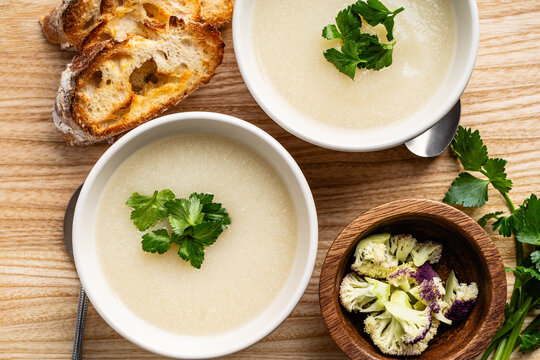 Cauliflower cream soup with grilled bread and cilantro on rustic wooden background