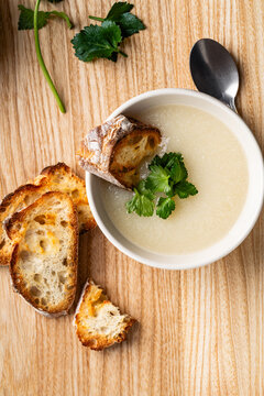 Cauliflower cream soup with grilled bread and cilantro on rustic wooden background
