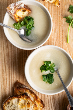 Cauliflower cream soup with grilled bread and cilantro on rustic wooden background
