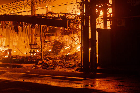 Devastating structure fire burns intensely in an Cilacap urban landscape with a dark atmosphere. Suitable for emergency response materials.