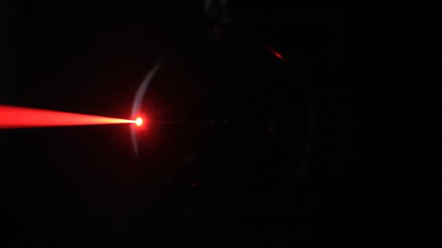 A focused red laser beam penetrates a clear glass sphere containing a dynamic, swirling cloud of white particles. The light illuminates the internal structure, which gradually fades and disperses ove