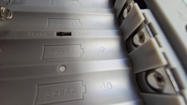 Close-up of an empty double A (AA) battery compartment with polarity markings and battery type selector switch.