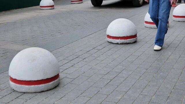 Pedestrian walking along a city sidewalk with bollards separating a car