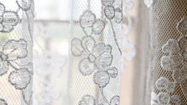 Closeup medium shot of sheer white Raschel lace curtain fabric showcasing delicate floral patterns and fine texture ideal for elegant drapery panels.
