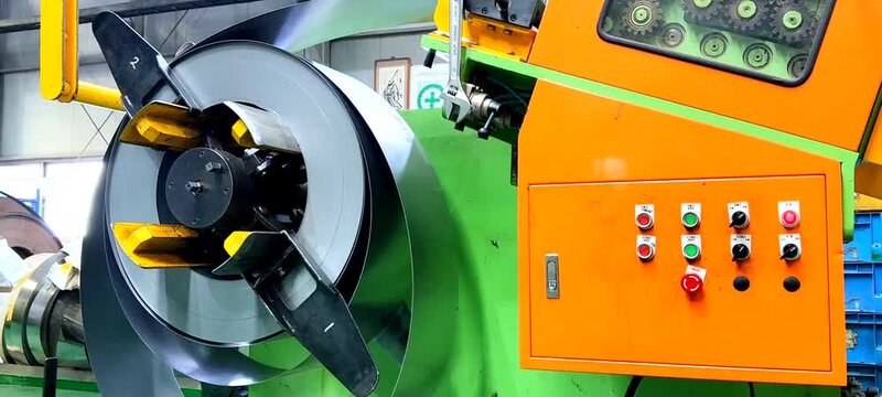 Industrial metal coil uncoiling on a decoiler machine in a factory.
