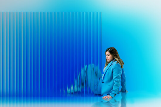 Woman leaning beside blue translucent 3D panel in studio setting