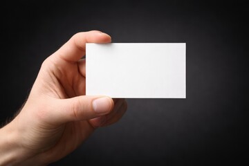 Obraz premium Hand holding a blank white business card against a simple dark background