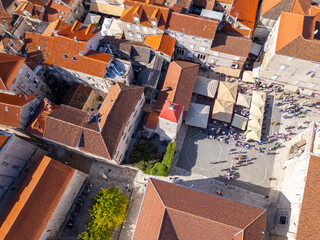 aerial view of a historic square with cafes, umbrellas and stone buildings inside the medieval old town of Trogir, Croatia