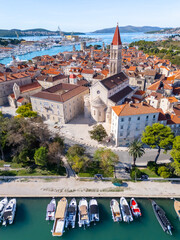 Scenic drone view of Trogir old town with cathedral, marina, yachts and Adriatic coastline surrounded by greenery and blue sea