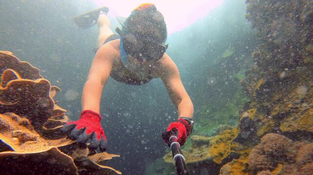 underwater selfie in ocean view of an asian woman female wearing bikini fin snorkel mask swimming free diving holding breath through narrow coral passages debris water exploring adventure marine life