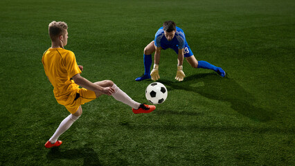 Fototapeta premium Soccer striker shooting ball against goalkeeper during match. Concept of scoring attempt, offensive play, football competition, sports advertising, match highlights, and editorial content.