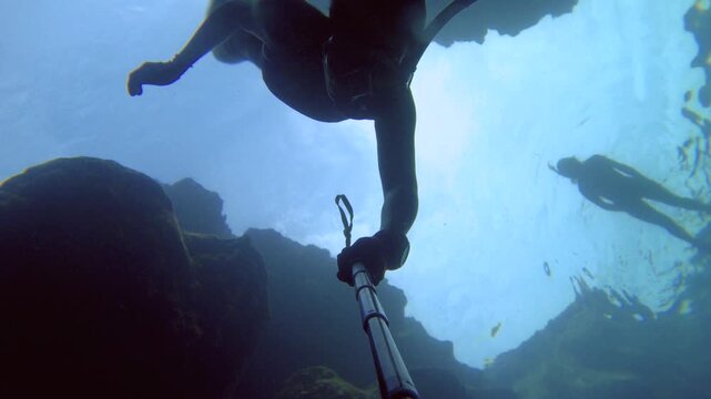selfie of an asian female woman wearing bikini snorkel mask fin free diving down into the water from bottom to top view in dark atmosphere surrounding by coral reef look up to diver silhouette surface