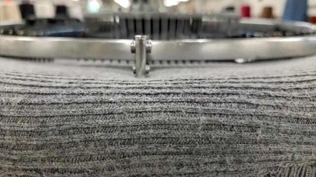 Detailed view of ribbed circular jersey fabric being produced emphasizing alternating raised and recessed rows with a tactile stretchy texture in a fabric manufacturing setting.