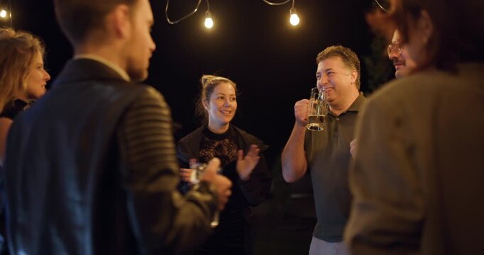 Friends Gather Outdoors at Night, Enjoying Drinks, Conversation, and the Warm Glow of String Lights