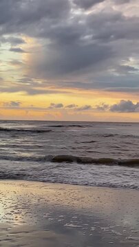 Calm ocean waves rolling onto a sandy beach during a colorful sunset. Dramatic clouds in the sky, warm light on the horizon, peaceful natural seascape, evening atmosphere, nature background, no people