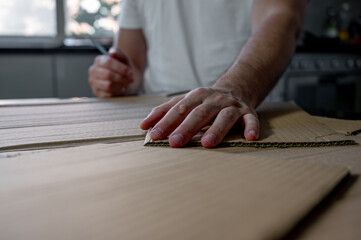 Close-up of hands crafting a cardboard sword on a table using cardboard, colored paper, and glue. DIY handmade project, creativity and imagination concept, eco-friendly hobby and recycled materials. 