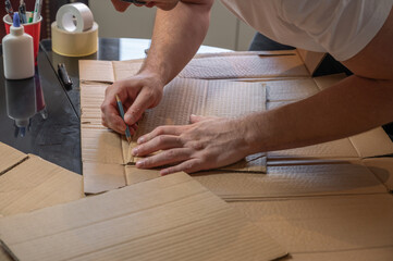 Man crafting a cardboard sword at a table using cardboard, colored paper, and glue. DIY handmade project concept, creativity, imagination, hobby, and eco-friendly low-budget craft.