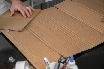 Close-up of hands working on a cardboard prototype at a desk. Startup project concept, product development, prototyping process, creativity, and innovation. Hands-on work, no face visible.