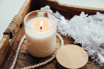 A massage candle in a glass with a spout, on a wooden tray, decorated with a pearl necklace and...