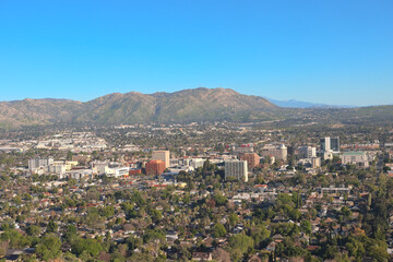 Obraz premium Panoramic view of downtown Riverside, California with city buildings, residential neighborhoods, and mountain foothills under a clear sky.