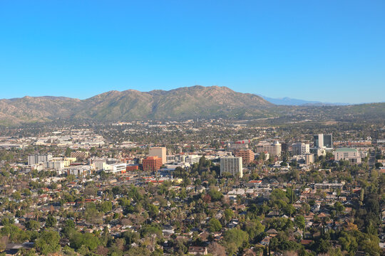 Panoramic view of downtown Riverside, California with city buildings, residential neighborhoods, and mountain foothills under a clear sky.