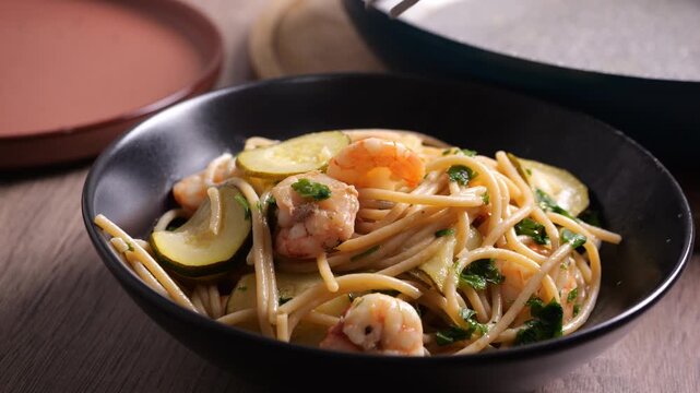 Il cuoco mette i gamberetti e le zucchine come guarnizione sugli spaghetti