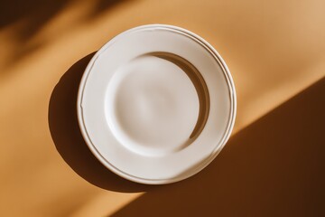 Overhead Shot of Empty White Plate with Golden Rim on Tan Surface under Sunny Lighting with Shadows Creating a Minimalist Neutral Still Life