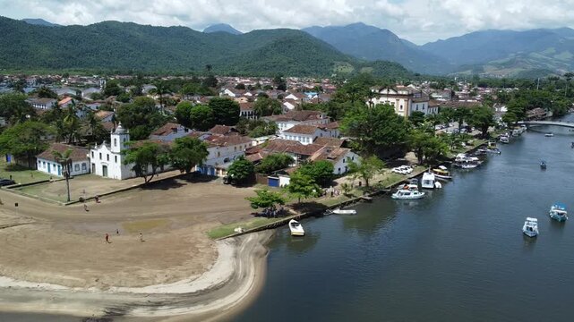 Drone circling from the river Pereque Acu, slowly revealing Paraty historical centre, the beach by the river and the mountains with the Atlantic forest that surrounds this historical city