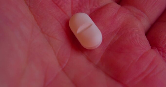 Macro shot of a closed fist unfurling to expose a single medicinal capsule on an open palm.