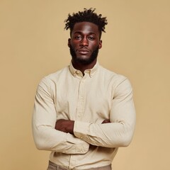 A man is posing with arms crossed in a studio. He is wearing a button-up shirt with a neutral background
