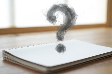 Smoke question mark rising from blank notebook page, for concept or idea generation, isolated on blurred background