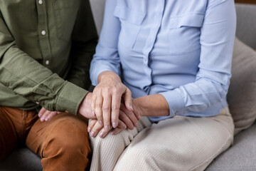 Mature man gently placing his hand over an older woman's hand, conveying care, empathy, and a...
