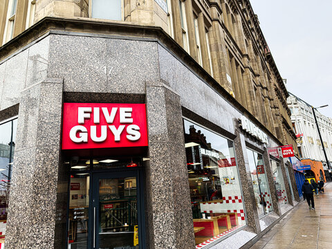 Five Guys restaurant on a bustling Manchester street exterior with bold red sign