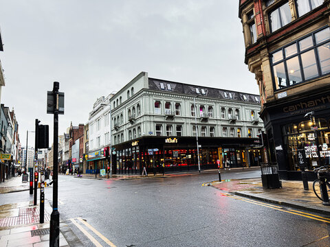 Busy Oldham street corner in Manchester with shops, pedestrians, and rain slicked pavement