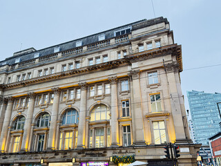 Naklejka premium Historic city building in Manchester with ornate columns and busy Cross street life by shopfronts