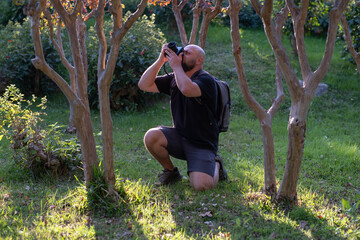 Man Taking Photos in a Public Park. Photographer Capturing Moments in Urban Park. Male Photographer Using Camera Outdoors in Park. Man with Camera Photographing Nature in Park.