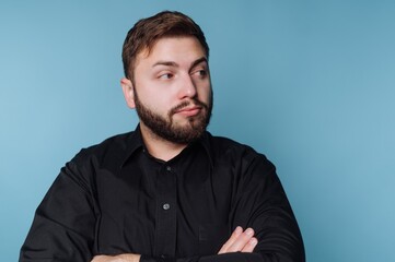 Obraz premium Man with beard stands against blue background with arms crossed during indoor session