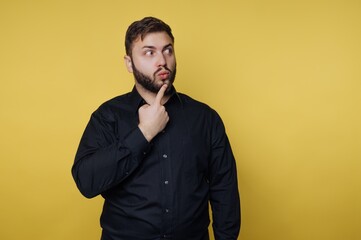 Fototapeta premium Man with beard in black shirt thinking and looking to the side in front of yellow background during daytime